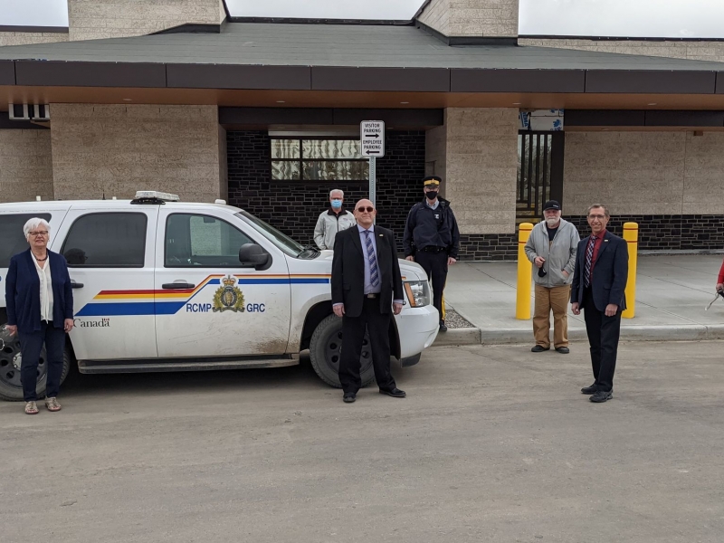 Town Council members standing in front of new RCMP building next to parked police SUV
